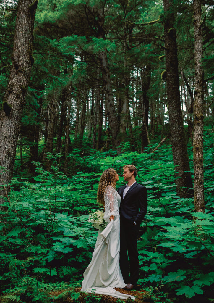 Romantic couple immersed in the serene beauty of an Alaskan forest, surrounded by towering trees and lush greenery. The pair shares a joyful moment, embracing each other amidst the breathtaking wilderness. A perfect blend of love and nature in the heart of Alaska's enchanting forests.